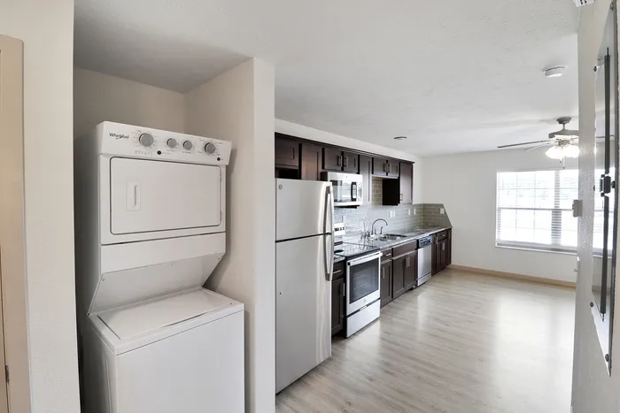 Modern kitchen with stainless steel appliances, dark wood cabinets, and a convenient in-unit washer and dryer, complemented by natural light from a large window.