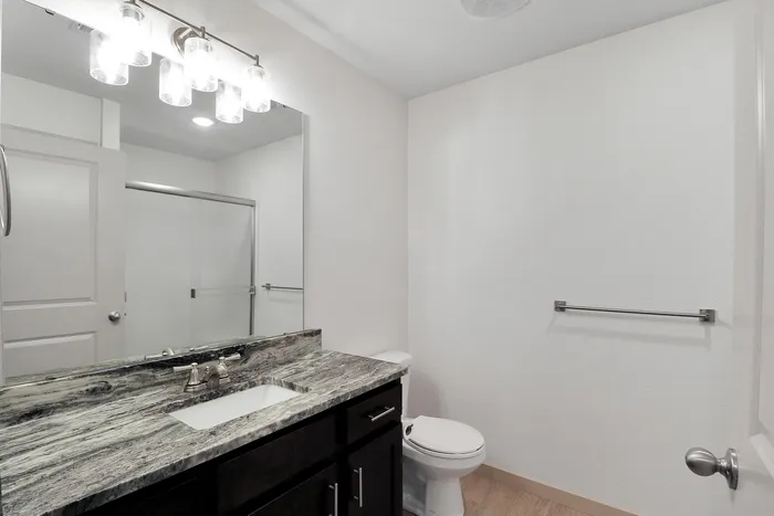 Bright and modern bathroom featuring a sleek marble countertop, elegant light fixtures, and a spacious glass shower.