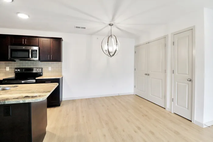 Modern kitchen with sleek dark cabinets, stainless steel appliances, and an elegant chandelier, offering a stylish and inviting space.