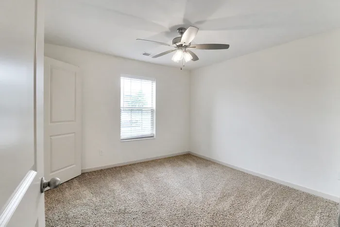 Bright and airy bedroom with plush carpeting, large window, and ceiling fan, offering a cozy retreat.