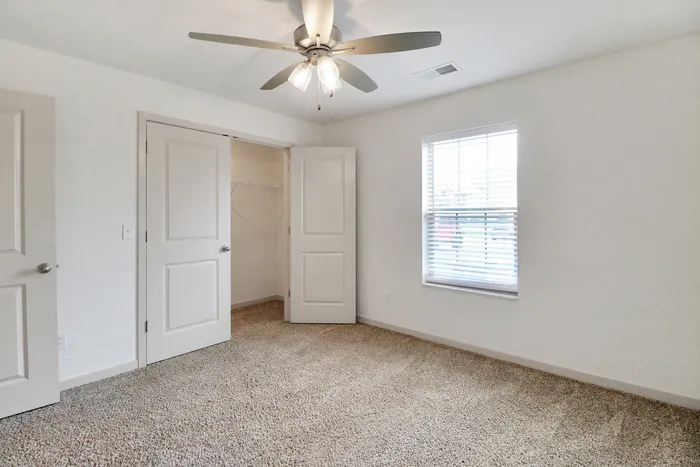 Bright bedroom with plush carpeting, modern ceiling fan, and generous closet space.