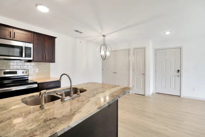 Modern kitchen with sleek granite countertops, stainless steel appliances, and stylish lighting in a bright, open-concept apartment.