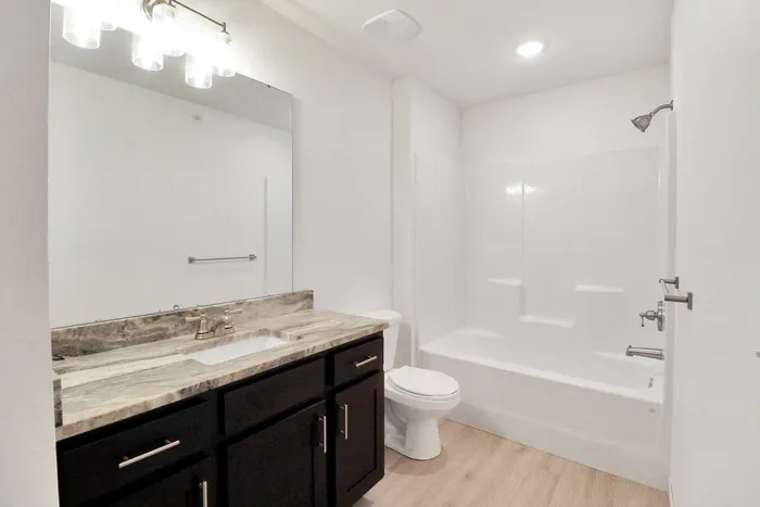 Bright, modern bathroom with elegant marble countertop, sleek dark vanity, and inviting tub-shower combination, perfect for relaxing moments.
