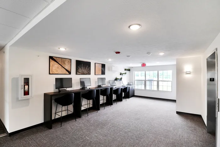 Bright and modern communal workspace with stylish computer stations, artistic wall decor, and large windows in a contemporary apartment building.