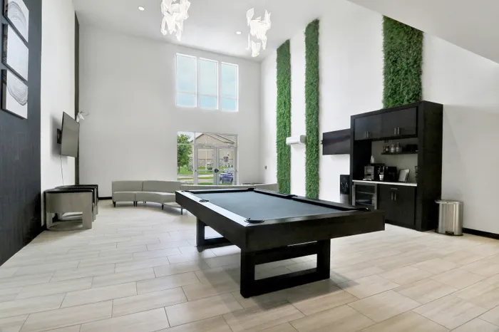 Bright and modern game room featuring a sleek pool table, elegant lounge seating, and lush vertical greenery.