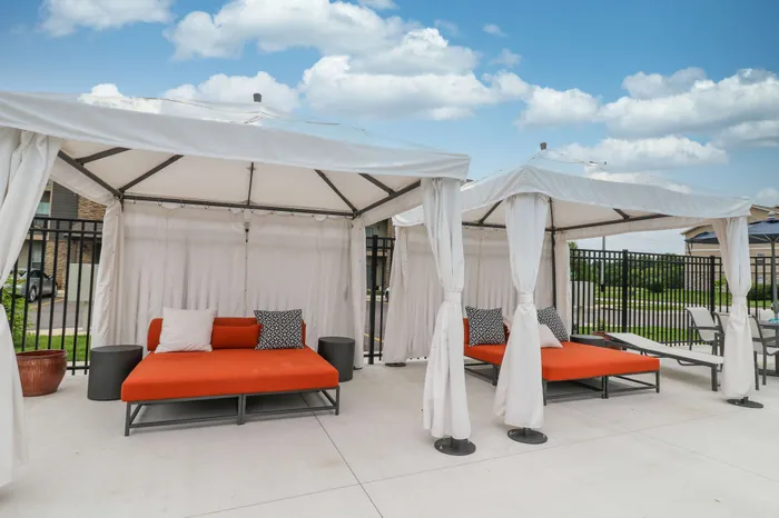 Chic outdoor lounge area with vibrant orange daybeds under elegant white cabanas, perfect for relaxation and socializing.