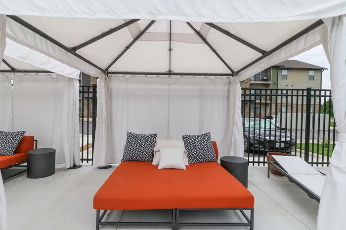 Inviting outdoor cabana featuring a vibrant orange daybed with stylish patterned pillows, perfect for relaxing in a serene setting.