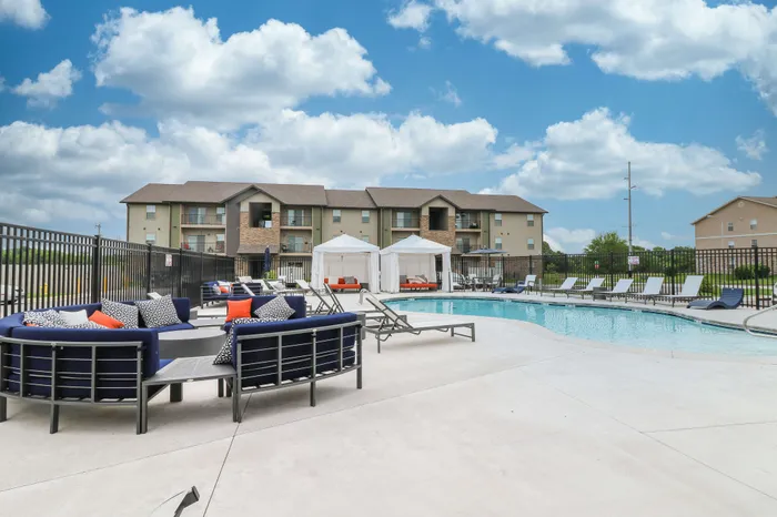 Inviting apartment complex with a luxurious outdoor pool, stylish loungers, and elegant cabanas under a bright blue sky.
