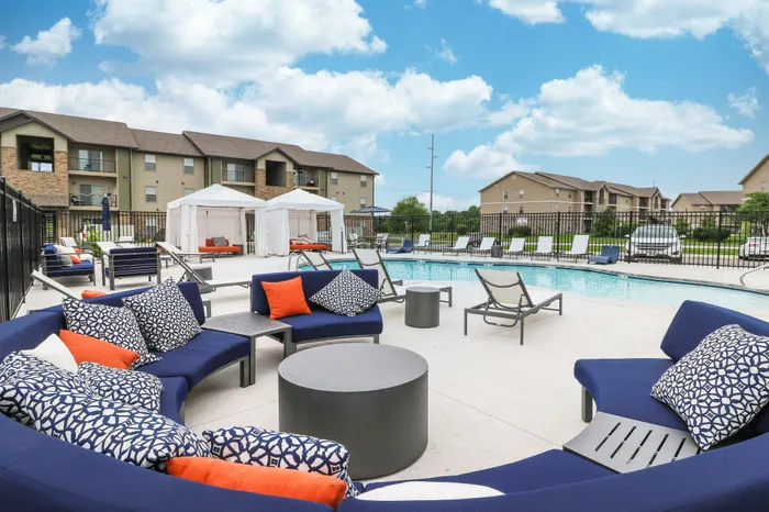Luxurious apartment complex featuring a sparkling pool, elegant cabanas, and stylish outdoor seating with vibrant cushions, ideal for relaxation and social gatherings.