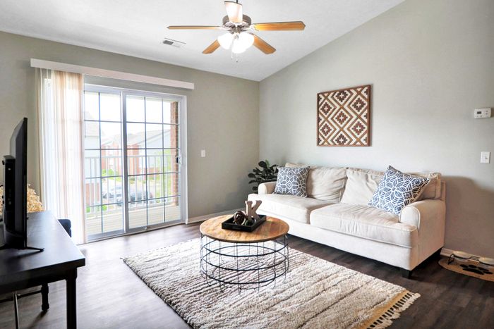 Bright and inviting living room with a cozy cream sofa, stylish patterned pillows, and a chic round coffee table; large sliding glass doors open to a scenic balcony view.
