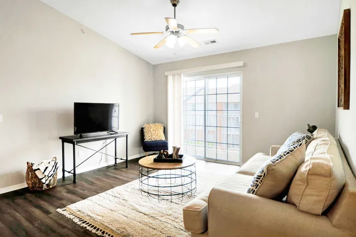 Bright living room with modern furnishings, a cozy sofa, large TV, and sliding glass doors leading to a balcony.