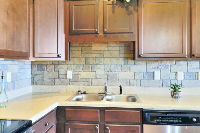 Elegant kitchen with modern cabinetry, stone tile backsplash, and stainless steel sink, complemented by sleek countertops and integrated dishwasher.