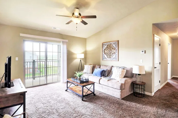 Bright and inviting living room with plush beige sofa, decorative wall art, and expansive sliding glass doors opening to a scenic balcony view.