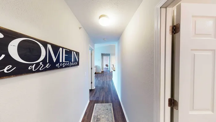 Inviting hallway with elegant flooring leading to a bright, open living area, enhanced by inspirational wall art.