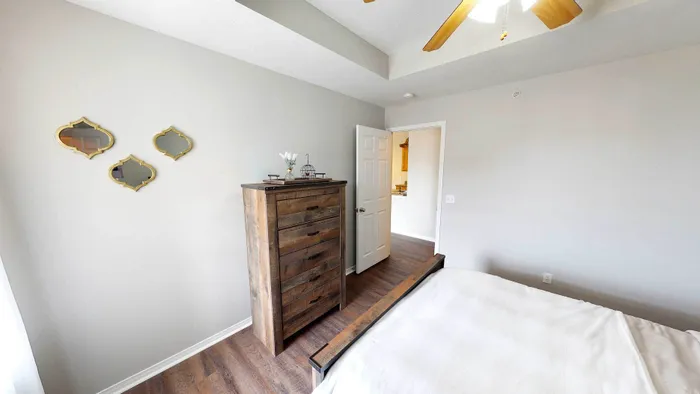Bright and inviting bedroom with modern wall decor, a rustic wooden dresser, and elegant ceiling fan, highlighting stylish apartment living.