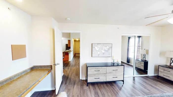 Bright and inviting apartment room with chic wooden flooring, sleek dressers, and modern decor, featuring large mirrors and abundant natural light.