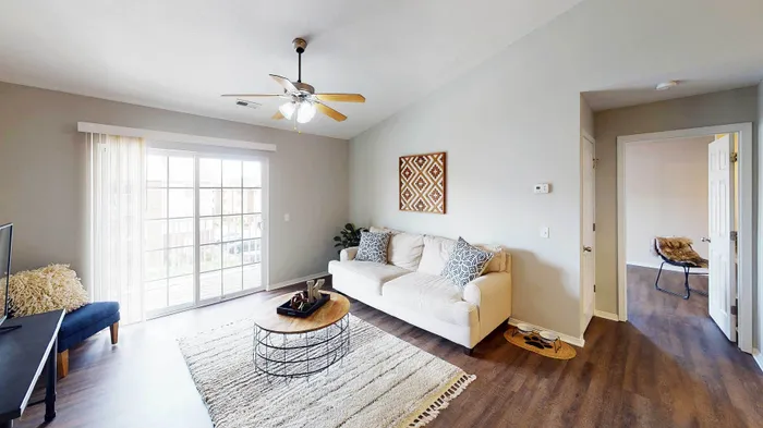 Bright and modern living room with a cozy beige sofa, elegant wooden coffee table, and expansive sliding glass doors leading to a balcony. A perfect space for relaxation and entertaining.