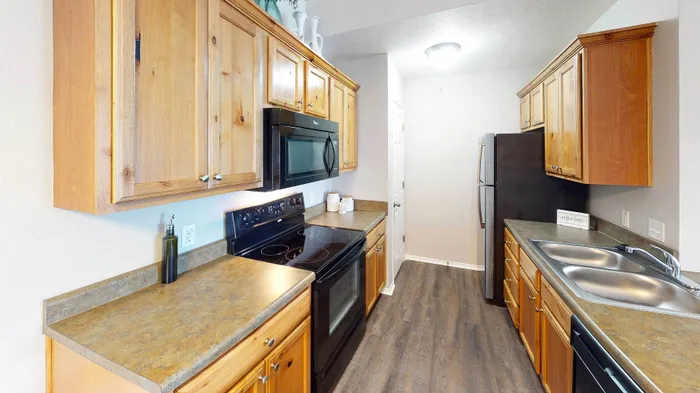 Contemporary kitchen with sleek black appliances, elegant wood cabinetry, and chic laminate flooring, offering a blend of functionality and style.