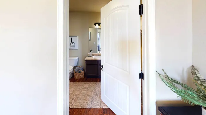 Inviting bathroom view from an open door featuring a modern vanity, elegant decor, and warm wooden flooring.