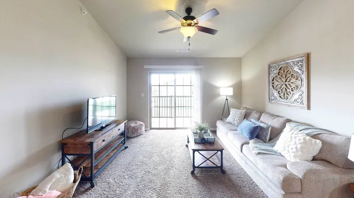 Inviting living room with a comfy beige sofa, chic wall art, and large sliding glass doors flooding the space with natural light.