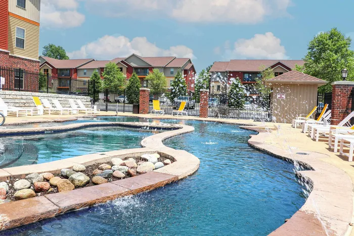 Luxurious outdoor pool area with elegant curved design, surrounded by vibrant townhouses and sun loungers, under a clear blue sky.