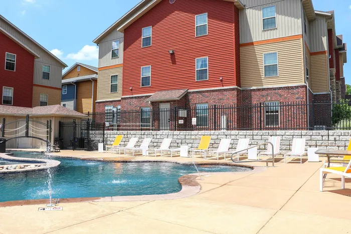 Inviting apartment complex with vibrant exterior overlooking a sparkling pool equipped with elegant fountains and stylish lounge chairs for relaxation.