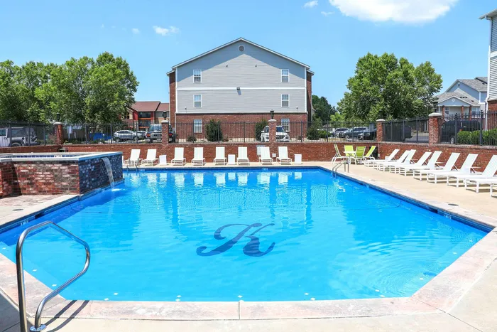 Inviting apartment complex pool with cascading waterfall, surrounded by sun loungers and scenic landscaping.