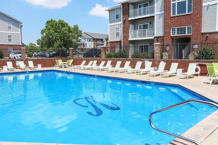 Inviting community pool with comfortable lounge chairs and brick-accented apartment backdrop, perfect for relaxation and leisure.