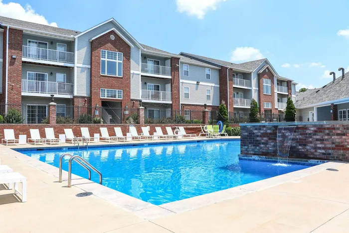 Beautiful apartment complex with a sparkling outdoor pool, surrounded by modern brick buildings and relaxing sun loungers.