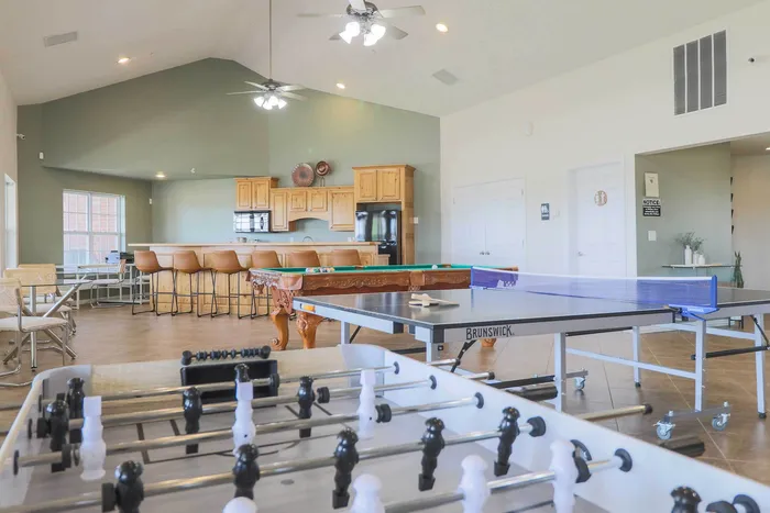 Inviting recreation room featuring modern bar seating, table tennis, pool table, and foosball in a spacious layout with abundant natural light.
