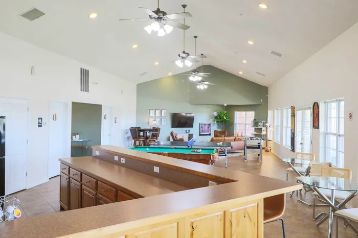 Bright and spacious community lounge with modern kitchen area, pool table, and comfortable seating, perfect for relaxation and social gatherings.