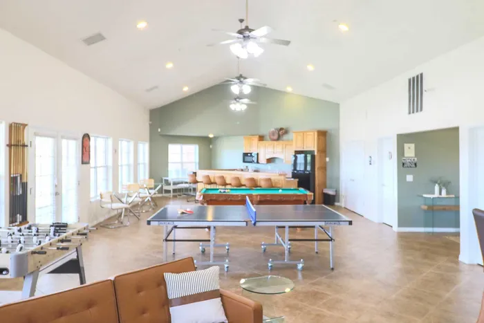 Spacious and modern recreational room featuring a ping pong table, foosball, and a cozy seating area with a stylish kitchen in the background.