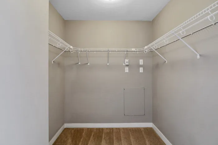 Spacious walk-in closet with ample shelving and neutral-toned carpet, perfect for organizing and storage.