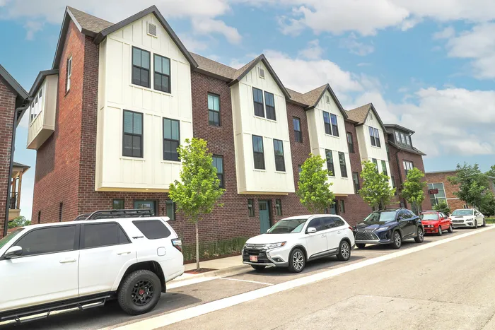 Charming brick townhouse complex with modern white panel accents and convenient street parking under a sunny sky.