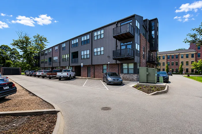 Modern apartment complex featuring sleek design with spacious balconies and convenient parking, surrounded by lush greenery and clear blue skies.