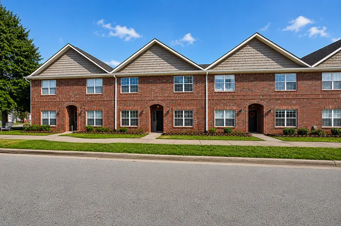 Charming red brick townhouse with inviting archways and large windows, nestled in a serene neighborhood with lush greenery.