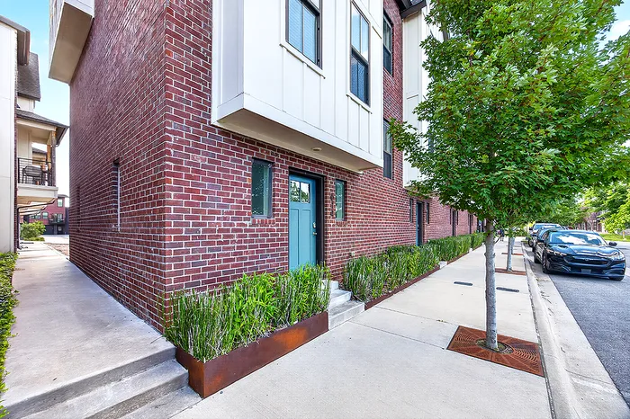 Charming brick apartment exterior with modern design, lush greenery, and tree-lined sidewalk offering an inviting urban living experience.