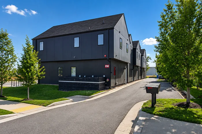 Modern townhouse exterior showcasing sleek black facade amidst lush greenery and a well-maintained driveway.