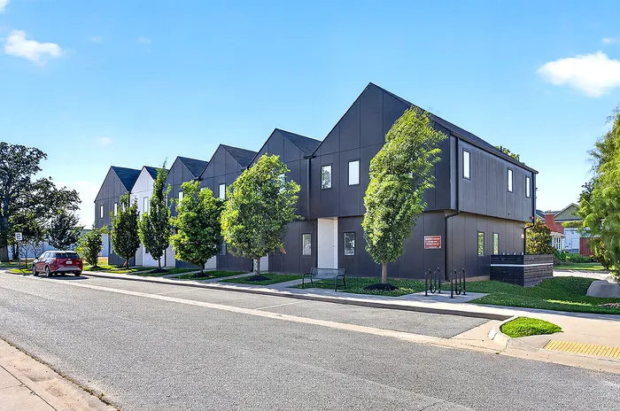 Charming row of modern townhouse apartments with sleek black exteriors, nestled in a lush green suburban setting.