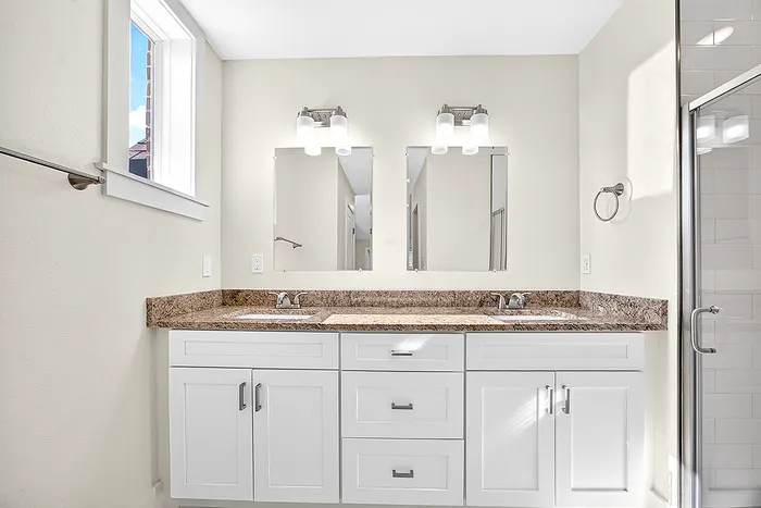 Elegant bathroom with double vanity, granite countertops, and modern fixtures, offering ample natural light.