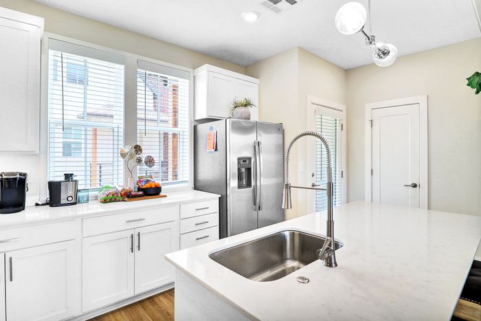 Bright and modern kitchen featuring sleek white cabinetry, stainless steel appliances, and a spacious quartz countertop with built-in sink.