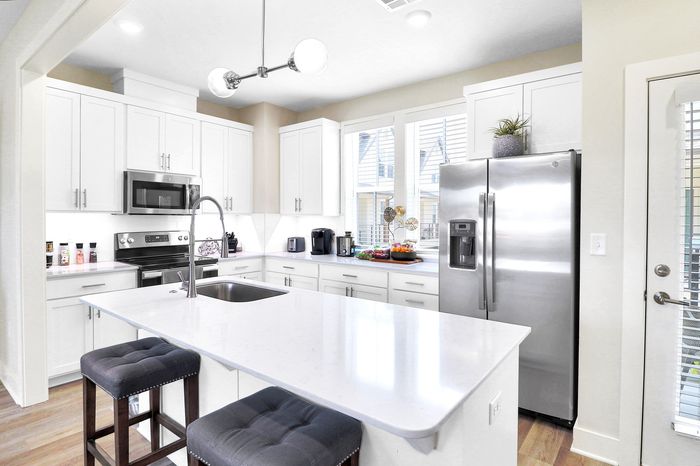 Bright and modern kitchen featuring sleek white cabinetry, stainless steel appliances, and a spacious island with bar stools.