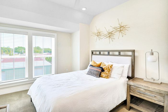 Bright and inviting bedroom with modern decor, featuring large windows, elegant bed with plush pillows, and stylish side table with a chic lamp.