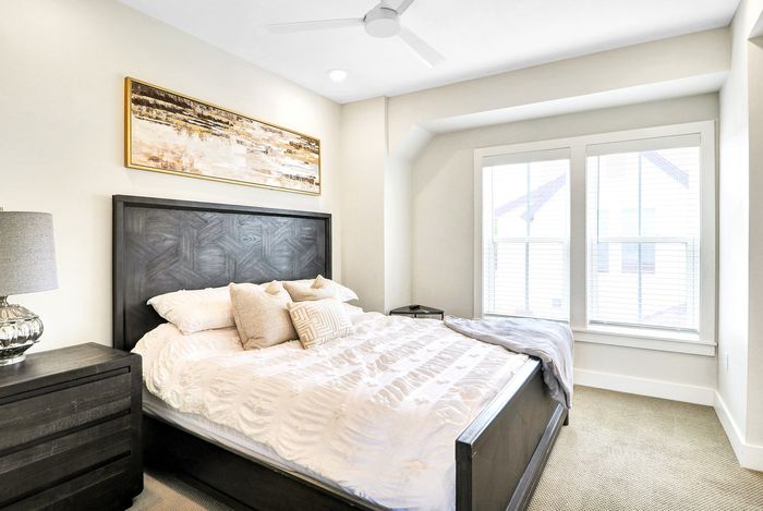 Bright and inviting bedroom with a plush bed, modern wooden headboard, and natural light streaming through large windows.