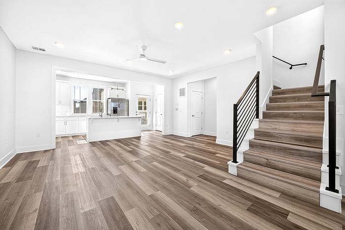 Bright and modern open-concept living area with sleek kitchen and elegant staircase, featuring stylish wood flooring and abundant natural light.