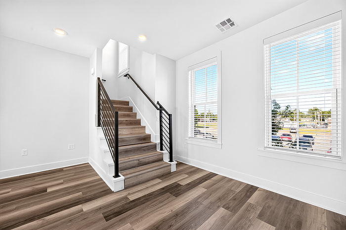 Bright and inviting stairway with sleek metal railing and large windows offering natural light, complemented by elegant wood flooring.