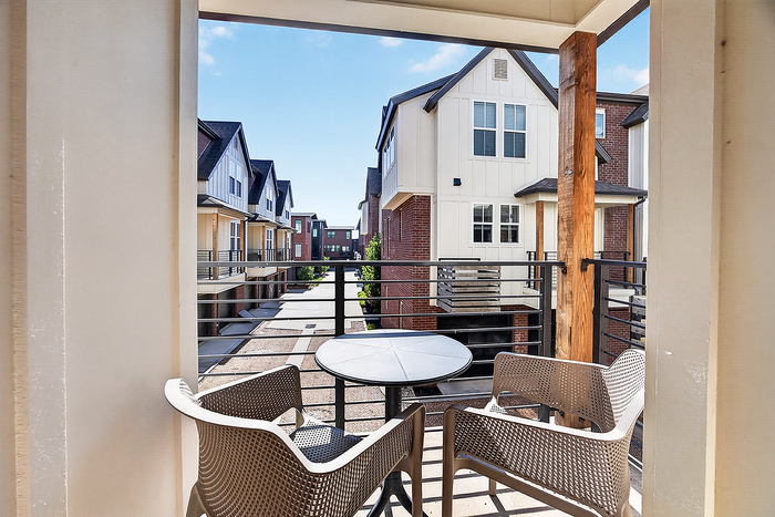 Charming balcony view from a modern apartment, showcasing stylish outdoor seating and picturesque townhouses under clear blue skies.