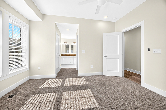 Bright and airy bedroom with plush carpeting, large windows, and a view into an elegant bathroom with double vanity.