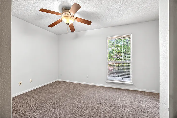 Inviting bedroom with plush carpet, bright natural light, and modern ceiling fan, offering comfort and style.