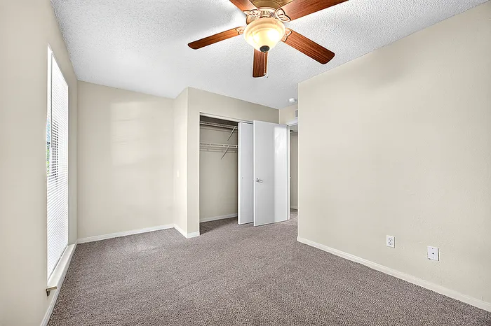 Bright, spacious bedroom with plush carpeting, ceiling fan, and ample natural light from a large window, offering a comfortable and inviting living space.